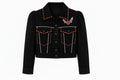 A black cropped denim jacket with red and white rhinestone embellishments, featuring a winged heart patch on the chest, on a solid white background.